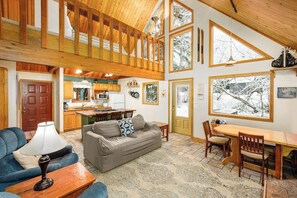 A spacious living area with a high ceiling, wooden beams, a dining table, and a sofa. - Two-bedroom Plus Loft Chalet w/ Mountain Views (Girdwood)