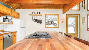 Cocina con encimera de madera, estufa, ollas colgantes y ventana con vistas nevadas.