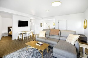 A modern living room with a grey sofa, a wooden coffee table, and a flat-screen TV mounted on the wall.