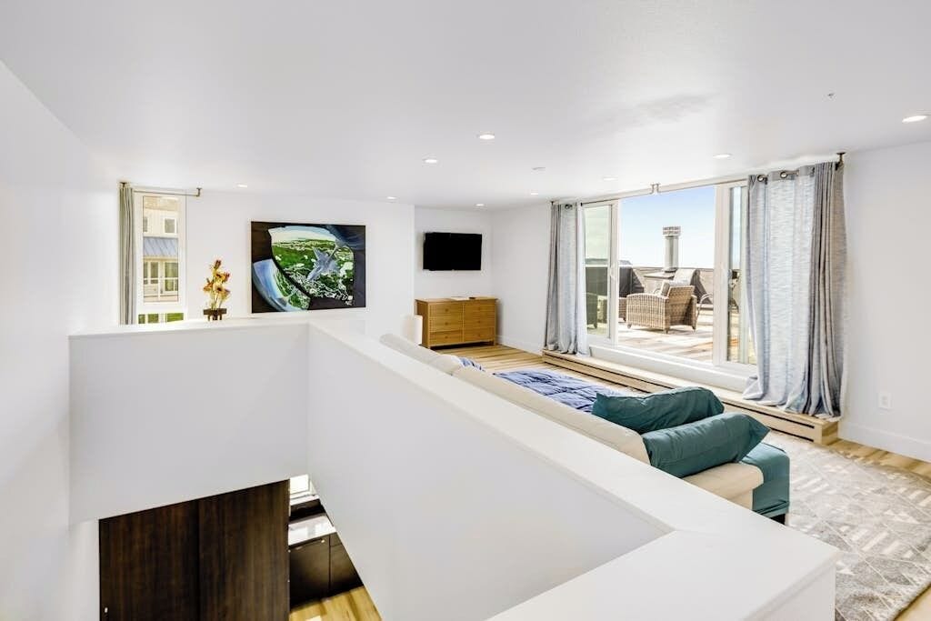 A modern living room with a sofa, a flat-screen TV, and a large window with curtains.