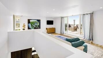A modern living room with a sofa, a flat-screen TV, and a large window with curtains.