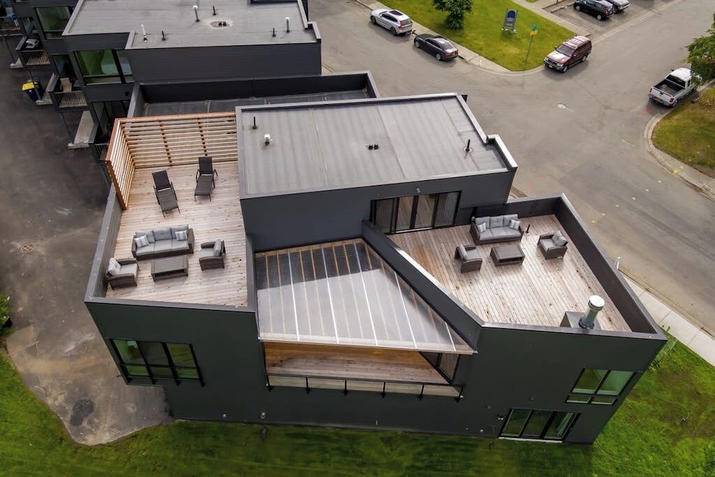 A modern multi-story building with a rooftop deck, large windows, and a parking area.