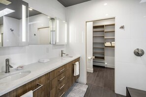 A modern bathroom with a large mirror, dual sinks, and a walk-in closet.