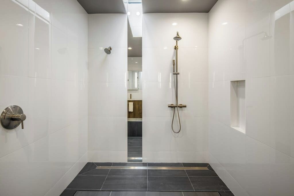 A modern bathroom with a walk-in shower, white tiled walls, and a dark floor.