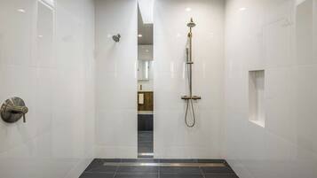 A modern bathroom with a walk-in shower, white tiled walls, and a dark floor.