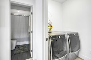 A compact laundry room with two front-loading washing machines, a toilet, and a shower area.