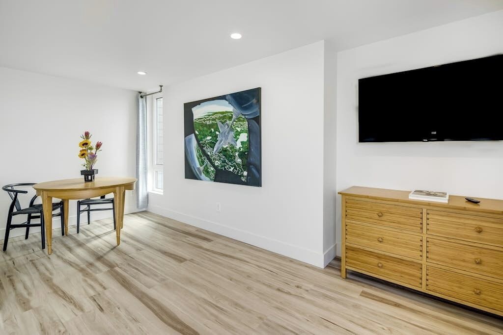 A modern living room with a dining table, a flat-screen TV mounted on the wall, and a wooden cabinet.