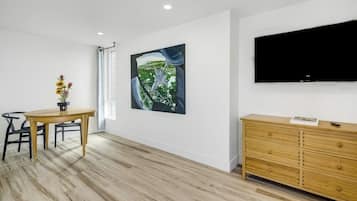 A modern living room with a dining table, a flat-screen TV mounted on the wall, and a wooden cabinet.
