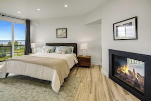 A bedroom with a bed, bedside lamps, a fireplace, and a large window with a view.