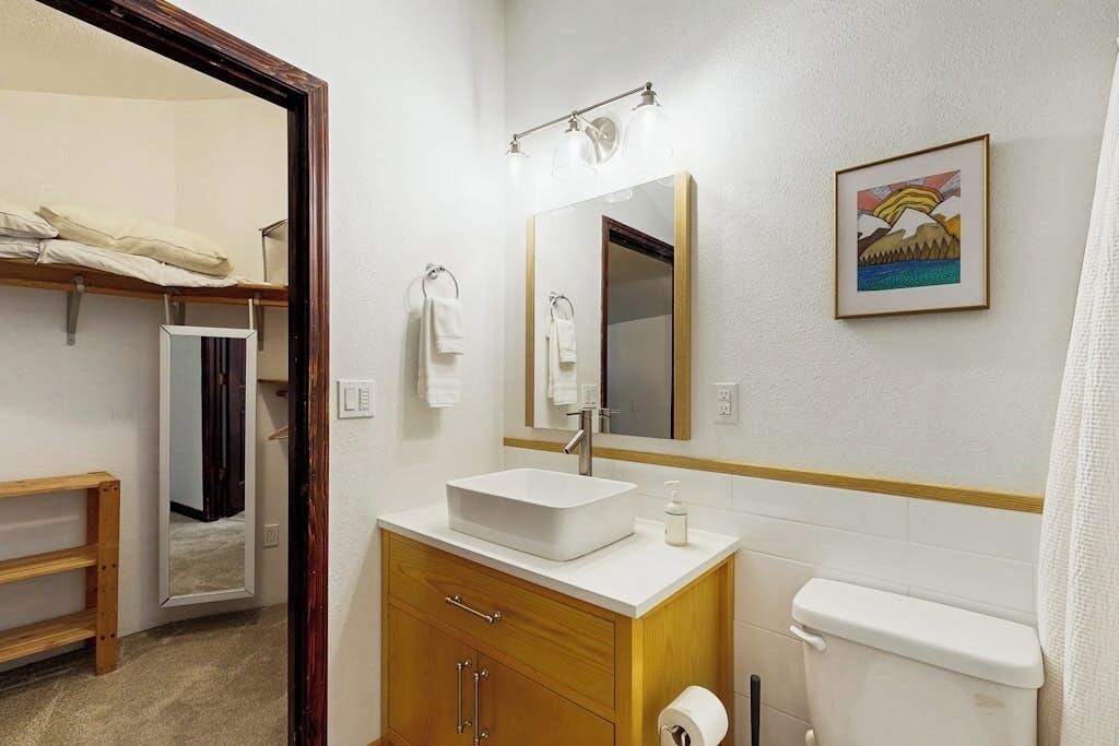 A compact hotel bathroom with a white sink, a mirror, a toilet, and a shower curtain.