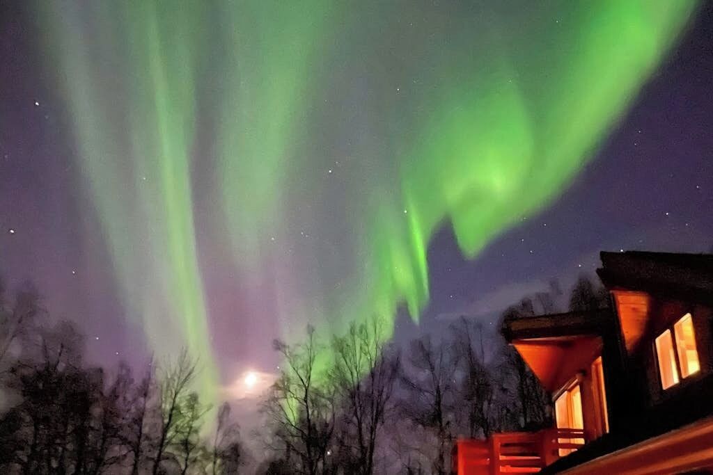 A cabin with a view of the night sky and aurora borealis.