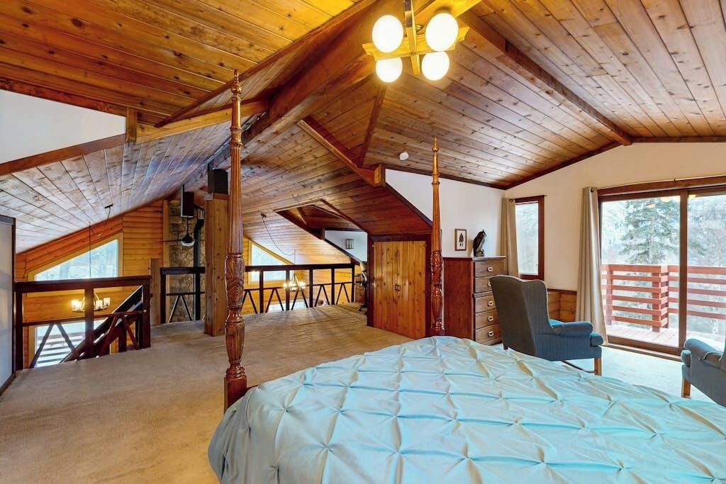 A high-ceilinged room with a bed, a chair, and a view of the outdoors.