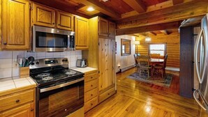 A kitchen with wooden cabinets, a stainless steel stove, and a microwave. - Remote 2BR Log Cabin Tucked Outside Anchorage (Eagle River)