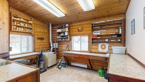 A log cabin interior with a kitchen area, wooden shelves, and a window. - Remote 2BR Log Cabin Tucked Outside Anchorage (Eagle River)