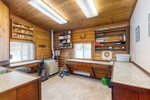 A log cabin interior with a kitchen area, wooden shelves, and a window. - Remote 2BR Log Cabin Tucked Outside Anchorage (Eagle River)