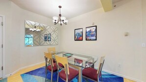 A dining area with a glass table, four chairs, a chandelier, and wall art.