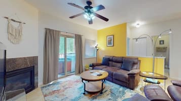 Una sala de estar con chimenea, ventilador de techo, sofá, mesa de centro y un comedor con lámpara.