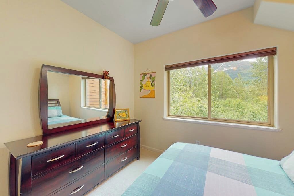 A bedroom with a bed, dresser, mirror, window, and ceiling fan.