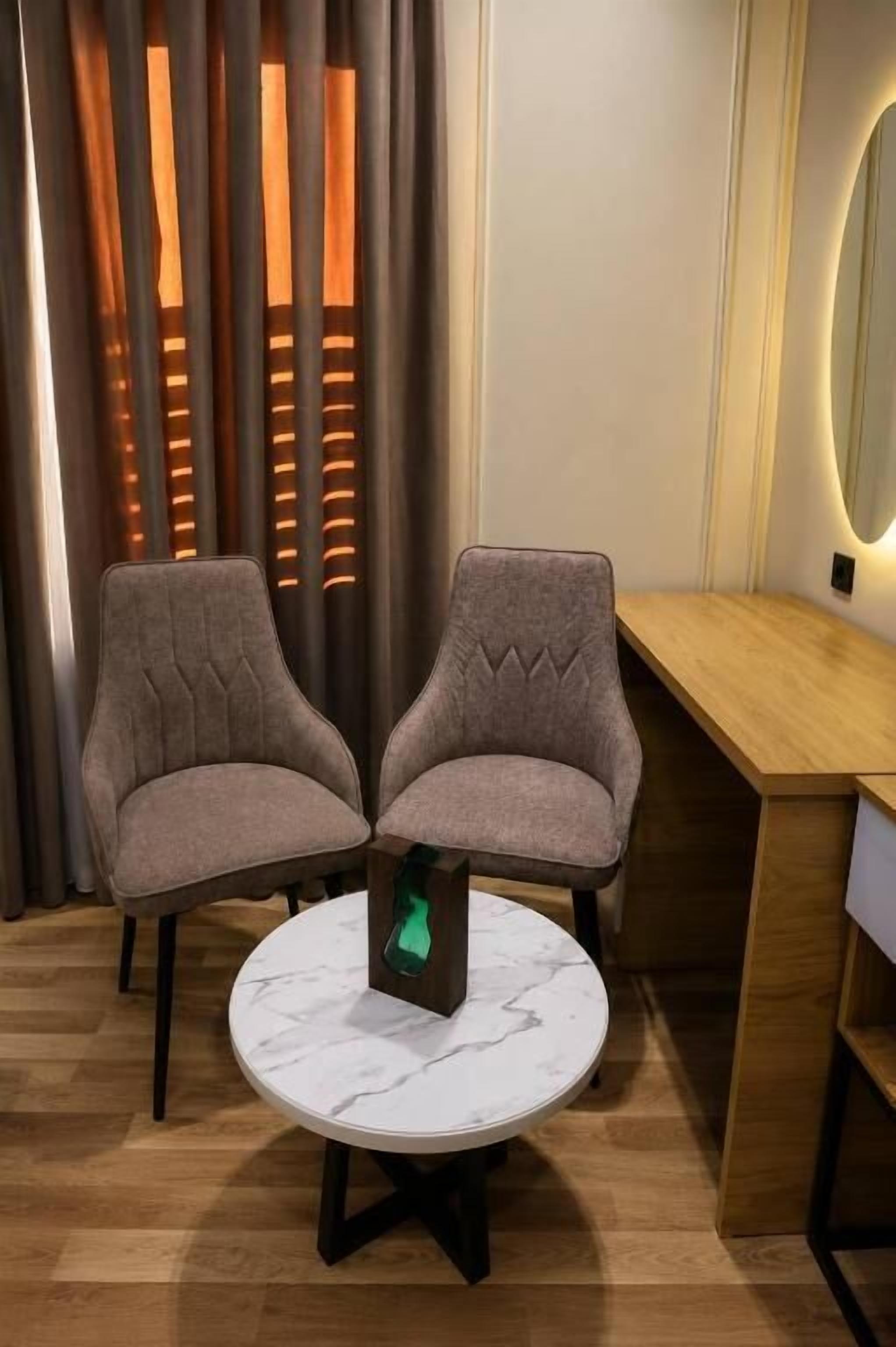 Una habitación con dos sillones tapizados, una mesa redonda con superficie de mármol y un escritorio de madera.
