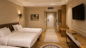 A hotel room with two beds, a TV, a desk, and a painting on the wall. - Amanat Prestige Hotel (Samarkand)