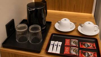 A coffee station with a black coffee maker, two cups, two saucers, and a tray with coffee packets.