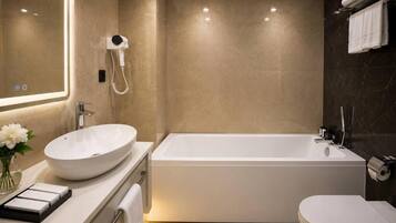 Une salle de bain moderne avec une grande baignoire, un lavabo rond et un sèche-cheveux fixé au mur.