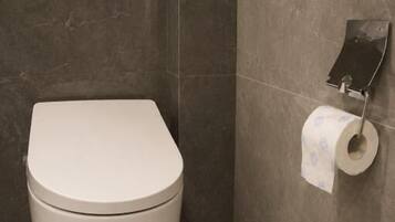 A toilet with a white lid, a wall-mounted toilet paper holder, and a marble-tiled wall.