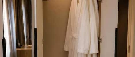 A walk-in closet with hanging robes, a shelf with shoes, and a storage box.