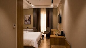 A hotel room with a bed, a desk, a chair, a television, and a painting on the wall. - Amanat Prestige Hotel (Samarkand)