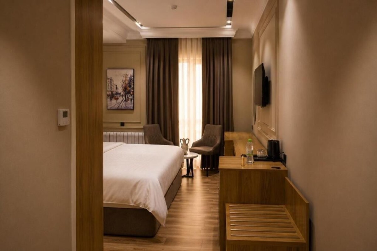 A hotel room with a bed, a desk, a chair, a television, and a painting on the wall.