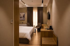 Una camera d'albergo con un letto, una scrivania, una sedia, una televisione e un quadro appeso al muro.