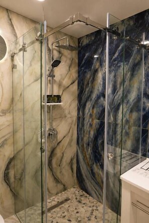 Una cabina doccia in vetro con un design murale in marmo.