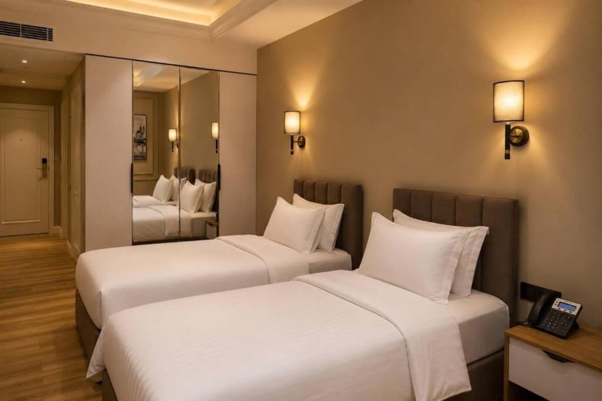 Una camera d'albergo con due letti, un comodino con un telefono e uno specchio.