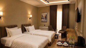 A hotel room with two beds, a desk with a coffee maker, a chair, a TV, and a painting on the wall. - Amanat Prestige Hotel (Samarkand)