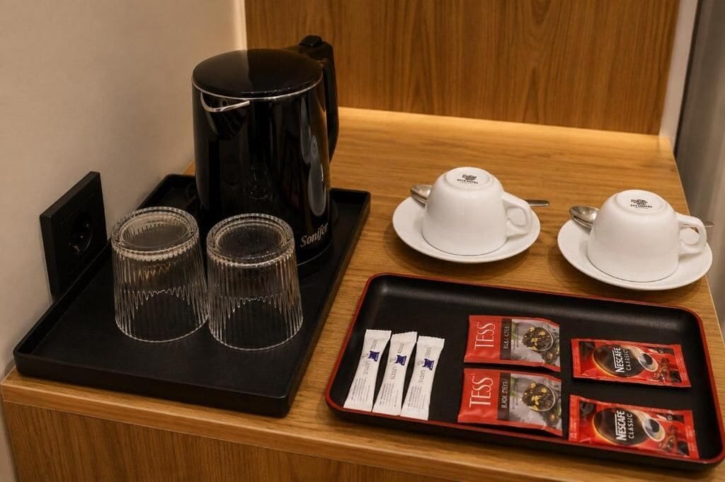 A coffee station with a black coffee maker, two cups, two saucers, and a tray with coffee packets.