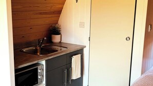 Une petite cuisine équipée d’un évier, d’une cuisinière et de placards, d’une petite plante en pot et d’une porte avec un porte-manteau.