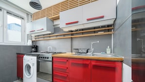 Een kleine keuken met een wasmachine, fornuis en rode keukenkastjes.
