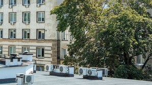 Een gebouw met meerdere ramen, airconditioningunits op het dak en een boom op de voorgrond.