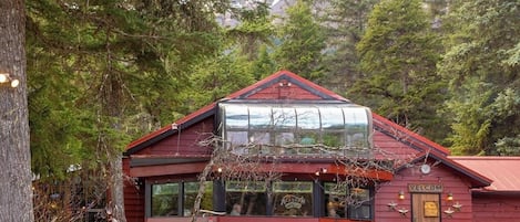 A red wooden building with a glass extension, a wooden door with a sign, and a natural forest backdrop.