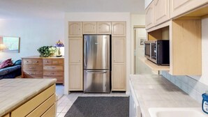 A compact kitchen with a built-in stainless steel refrigerator, wooden cabinets, a microwave, and a small countertop. - Slopeside Studio at Alyeska w/ Full Kitchen (Girdwood)
