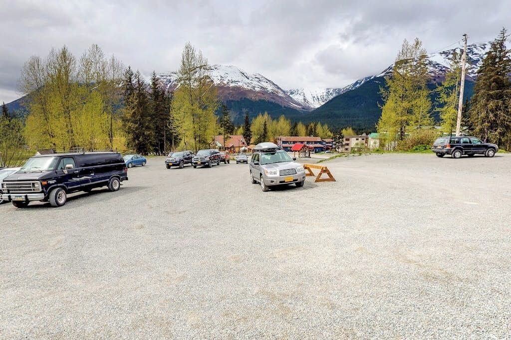 A parking lot with vehicles, a gravel surface, and a mountainous backdrop.