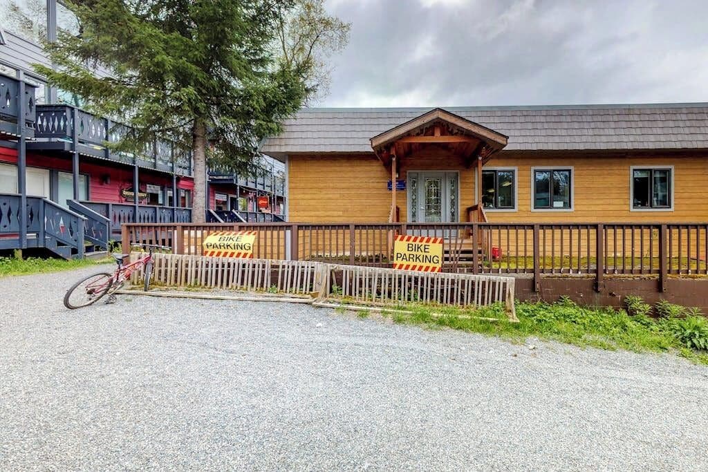 A building with a wooden facade and a covered porch, surrounded by a wooden fence with bike parking signs.