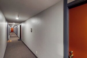 Un pasillo de hotel con piso alfombrado, una puerta con manija de latón y una lámpara en el techo.