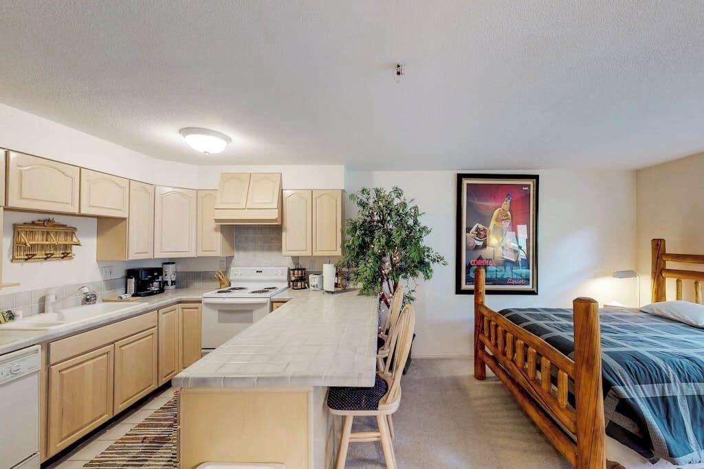 A compact kitchen with a dining area, a bed, and a poster on the wall.