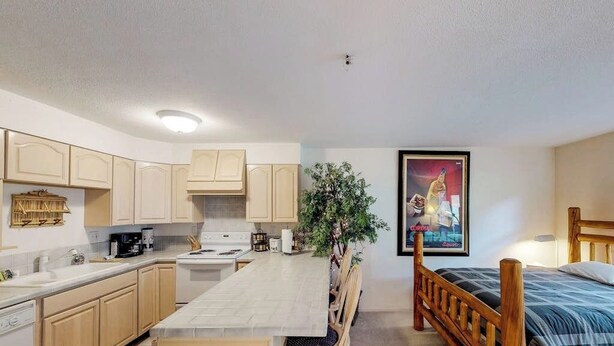 A compact kitchen with a dining area, a bed, and a poster on the wall. - Slopeside Studio at Alyeska w/ Full Kitchen (Girdwood)