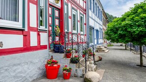 Un edificio europeo tradicional con fachada roja y blanca, una escalera adornada con plantas en macetas y una calle empedrada.