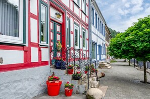 Ein traditionelles europäisches Gebäude mit roter und weißer Fassade, einer Treppe mit Blumentöpfen und einer Kopfsteinpflasterstraße.