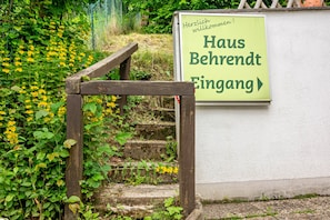 Eine Holztreppe führt zu einem Hauseingang, an dem Schilder mit der Aufschrift 'Haus Behrendt Eingang' und 'Herzlich willkommen!' befestigt sind.