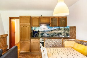 Habitación compacta con kitchenette, cama con ropa de cama estampada, lámpara colgante y televisor montado en la pared.