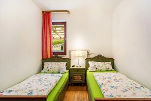 Una habitación pequeña y acogedora con dos camas individuales, una mesita de noche con lámpara y una ventana que da a un jardín.